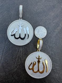 two silver and gold pendants with arabic writing on them, one has a coin