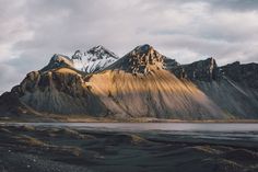 the mountains are covered in snow and brown grass, with water below them on a cloudy day