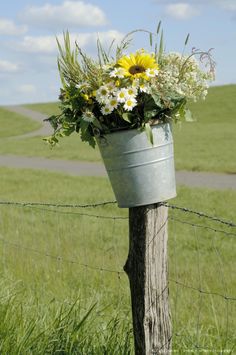 a metal bucket with flowers in it sitting on top of a fence post