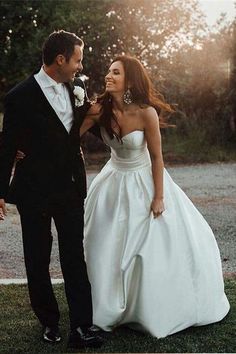 the bride and groom are walking together in their wedding attire, smiling at each other