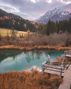 a person standing on a dock over a body of water with mountains in the background