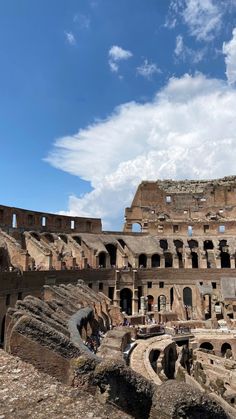 the interior of an ancient roman colliseum with people walking around it under a cloudy blue sky