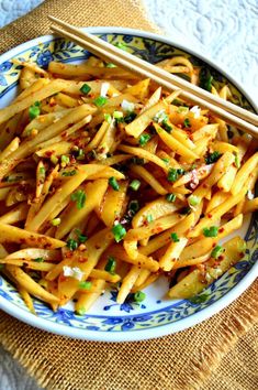 a blue and white plate topped with pasta and chopsticks