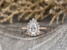 an engagement ring with a pear shaped diamond surrounded by smaller round diamonds on a wooden surface