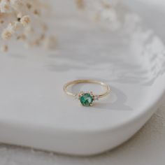 a gold ring with a green stone sits on a white surface next to dried flowers