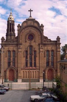 an old church with a cross on the top of it's steeple and cars parked in front