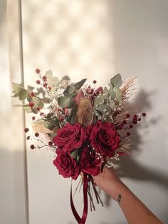 a bouquet of flowers is being held by a person's hand in front of a white wall