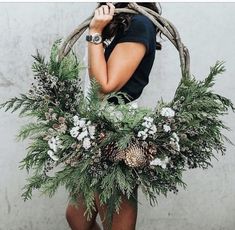 a woman holding a wreath with pine cones and evergreens