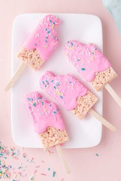 three popsicles with pink frosting and sprinkles on a white plate