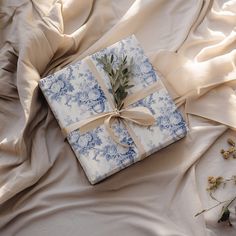 a wrapped present sitting on top of a bed covered in white and blue sheets with a ribbon