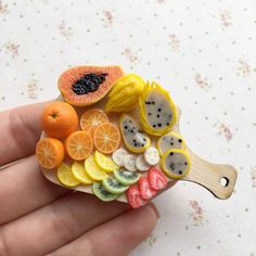 a hand holding a small wooden spoon with fruit slices and kiwis on it