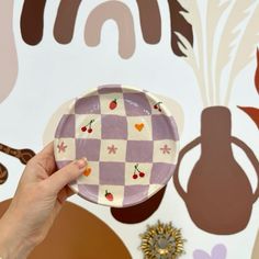 a hand holding a plate with cherries on it in front of a wall mural