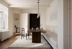 a room with a table, chairs and rugs on the floor in front of a window