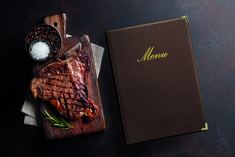 a steak on a wooden cutting board next to a menu and some salt in a bowl