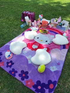 a hello kitty picnic blanket on the grass with food and toys laid out around it