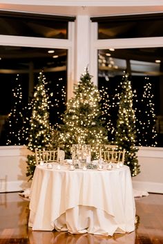 the table is set with candles and place settings in front of a christmas tree that has lights on it