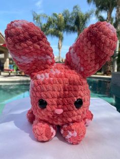 a red stuffed animal sitting on top of a white table next to a swimming pool