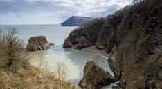 a river flowing between two large rocks on the side of a hill next to a body of water