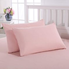 two pink pillows sitting on top of a bed next to a vase with flowers in it