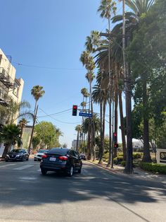 cars are driving down the street in front of palm trees and traffic lights on a sunny day