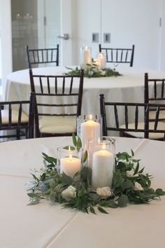 candles are lit on the table with greenery and flowers in front of white clothed tables