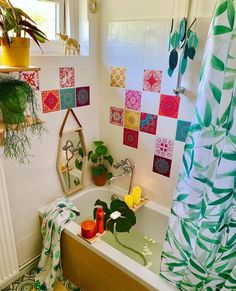 a bath tub sitting under a window next to a shower curtain and potted plants