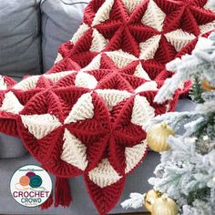 a red and white crocheted blanket sitting on top of a couch next to a christmas tree