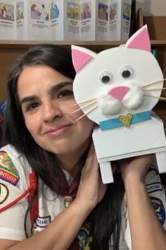 a woman holding up a paper cat in front of her face and smiling at the camera