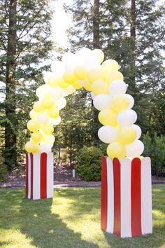 some yellow and white balloons are in front of red and white striped boxes on the grass