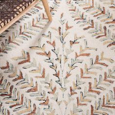 a white rug with multicolored leaves on it and a wooden chair in the background