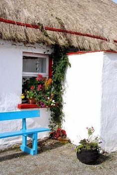 a blue bench in front of a thatched roof house with flowers on the window sill