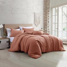 a bed with an orange comforter and pillows in a room next to a brick wall