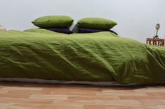 a green bed with two pillows on top of it and an end table in the background