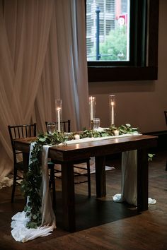 the table is set with candles and greenery for an elegant wedding reception in front of a window