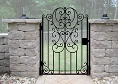 a wrought iron gate is open on a stone wall and walkway in front of a grassy area