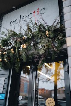 a christmas wreath is hanging on the front door of a building that has been decorated with greenery and pine cones