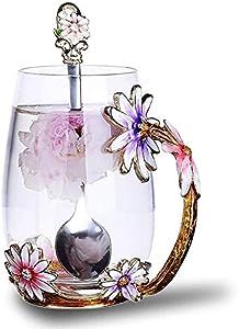 a glass filled with water and flowers on top of a white table next to a spoon