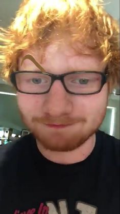 a man with curly hair and glasses is looking at the camera while wearing a black t - shirt