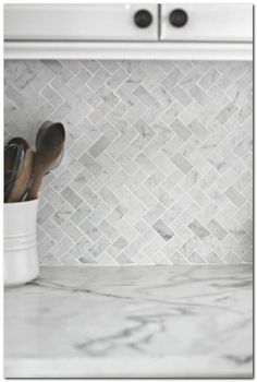 a white kitchen with marble backsplash and stainless steel oven mitts on the counter