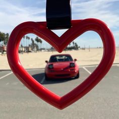 a heart shaped object in the middle of a parking lot next to a red car