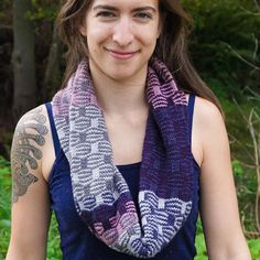 a woman with long hair wearing a purple and white knitted scarf in front of trees