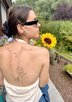 a woman with a sunflower tattoo on her back is sitting in front of a house