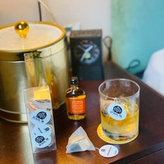 a wooden table topped with a glass filled with liquid next to a pot and bottle