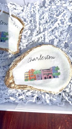 two wooden slices with the word charleston painted on them are in a box filled with shredded paper