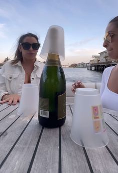 two women sitting at a wooden table with a bottle of wine in front of them