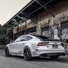 the rear end of a white car parked in front of a building with graffiti on it