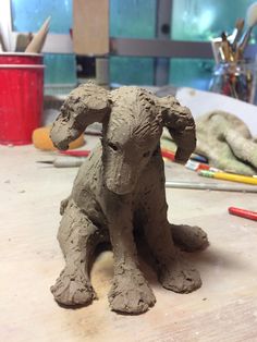 a clay dog sitting on top of a wooden table next to paintbrushes and pencils