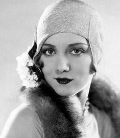 an old photo of a woman wearing a hat and fur stole around her neck with flowers in her hair