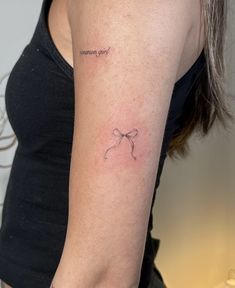 a woman's arm with a small bow tattoo on the left side of her arm