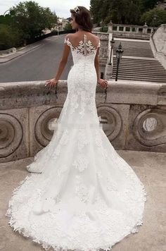 a woman in a white wedding dress standing on a balcony looking down at the street